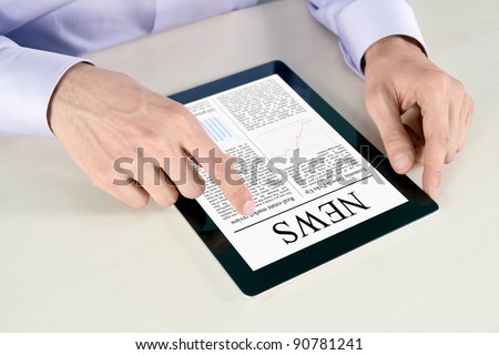 Businessman hands are pointing on contemporary digital tablet pc with latest news lying on table.