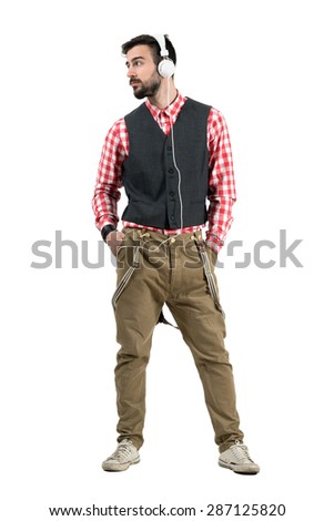 Relaxed hipster with hands in pocket listening mp3 player looking away. Full body length portrait isolated over white studio background.