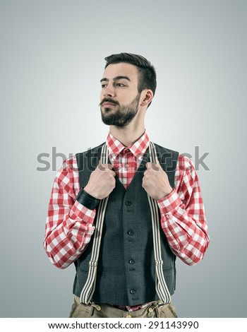 Desaturated portrait of standing young hipster model looking away with raised eyebrow while holding his pants suspenders.