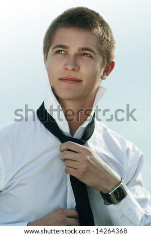 front view of a young handsome business man arranging his tie outdoors and looking at the sky