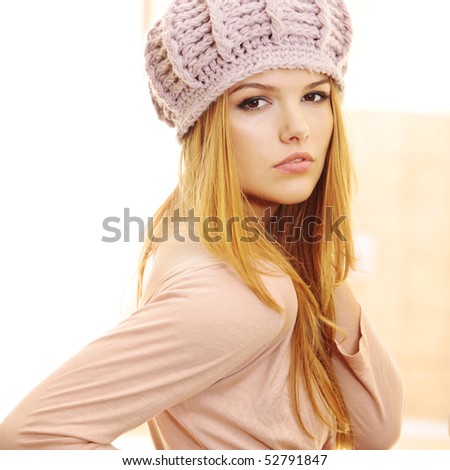 Over the shoulder profile of fashion model wearing warm pink hat and casual dress in beautiful interior at home looking at the camera