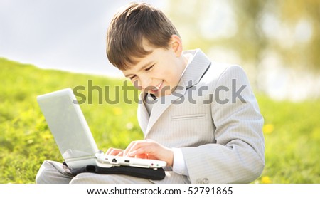 Business concept of mobility. Happy Child in suit with laptop outdoors in green meadow on a sunny day