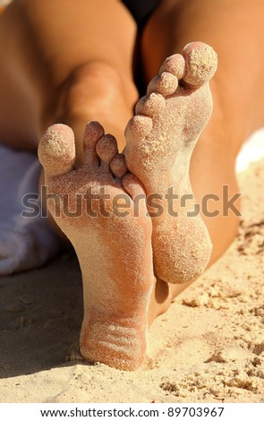 A sunbathing woman\'s sandy feet on the beach