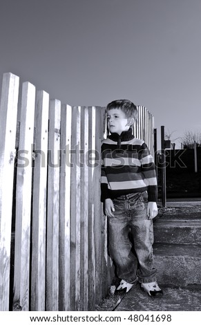 Lonely boy stands by a fence.