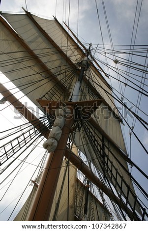 The rigging of a vintage sailing ship shows its sails full of wind at sea.
