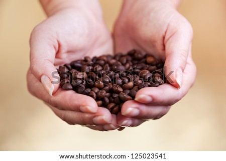Coffee beans in woman palms on golden background - closeup