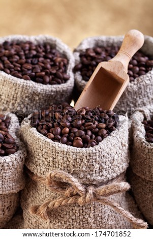 Roasted coffee in bags with wooden scoop on golden background.