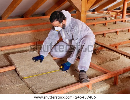 Man laying thermal insulation layer under the roof - measuring a mineral wool panel