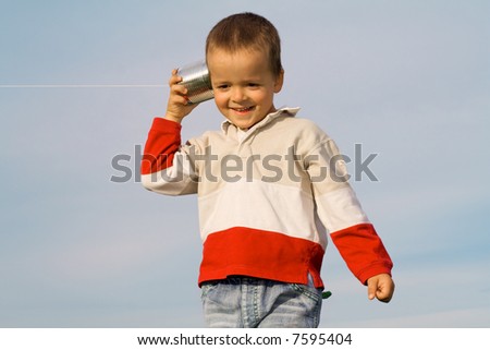 Boy with tin can and string phone playing outdoors - blue sky background