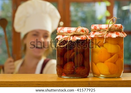 Happy woman chef with homemade canned fruit - focus on the jars