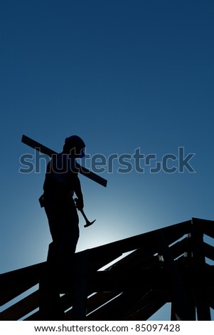 Builder working late on top of building holding hammer - in strong back light