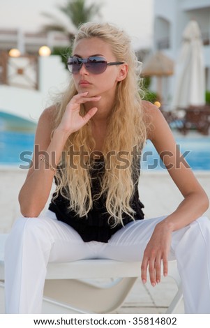Fashionable girl sitting on a pool background, summer outdoor shot