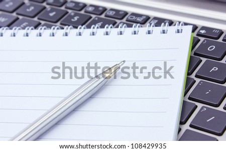 a notebook and pen lie on the keyboard of computer
