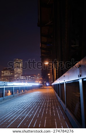 Pedestrian and bicycle path that is part of the metal transport truss bridge over Willamette River in Portland in twinkling night lights high-rise office buildings cyclist headlight on truss bridge.