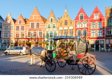 Bruges, Belgium - December 28, 2014: Horse-drawn carriage at the market square in Bruges. Famous colorful facades of houses in the medieval market square.