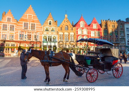 Bruges, Belgium - December 28, 2014: Horse-drawn carriage at the market square in Bruges. Famous colorful facades of houses in the medieval market square.