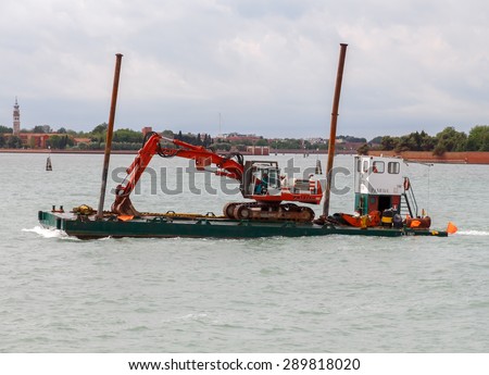 Venice, Italy - May 21 2015: Self-propelled barge transporting an excavator on the Venetian lagoon. The lagoon is constantly work is underway to deepen shipping channels.