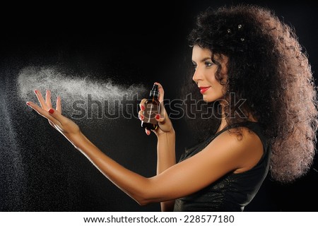 A portrait of a beautiful woman spraying perfume on black background