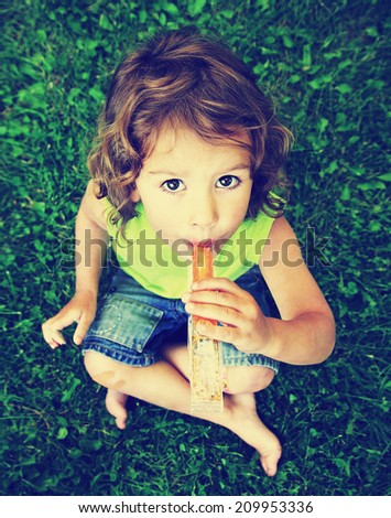 a young girl eating a frozen treat in the grass toned with a vintage retro instagram filter