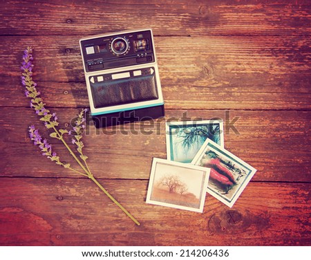 Vintage photo camera on a wooden table with some snapshots and a flower toned with a retro vintage instagram filter effect