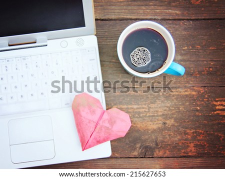 Laptop or notebook with cup of coffee and origami heart on old wooden table