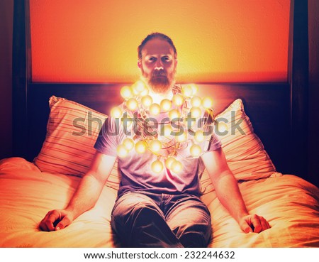 a man draped in christmas lights sitting on a bed looking depressed toned with a vintage filter