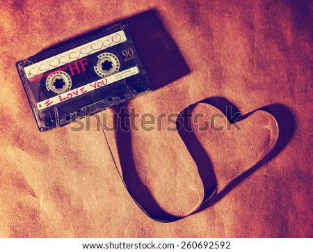 an old dirty grungy scratched up audio cassette tape in the shape of heart (focus on the words) on a brown paper texture background good for valentine\'s day or love greeting cards (SHALLOW DOF)