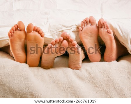 three people under the covers with feet showing in a bed