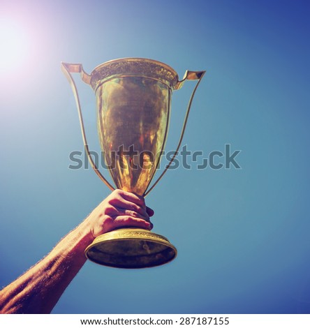 a man holding up a gold trophy cup as a winner in a competition toned with a retro vintage instagram filter effect app or action