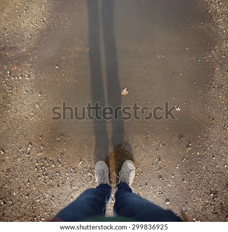 wide angle overhead shot of yellow and white boat or deck shoes in a muddy puddle with a long shadow of the legs