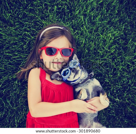 snapshot of a cute girl with sunglasses holding a chihuahua with goggles on in a grassy park or yard with a lawn toned with a retro vintage instagram filter effect app or action (focus on the dog)
