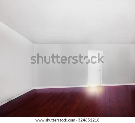a big empty white room with a hard wood stained floor and light leaking from under the closed door
