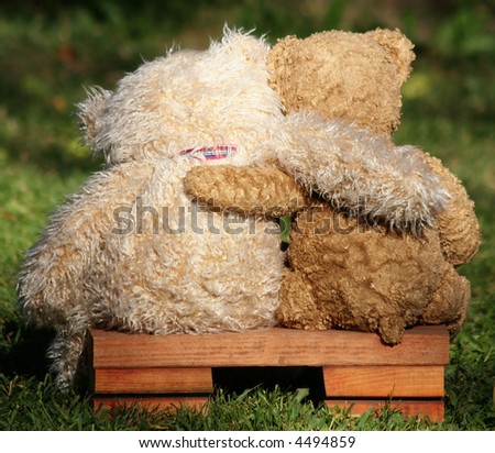 two teddy bears on a bench with arms around each other - stock photo