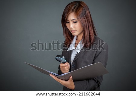 Asian businesswoman look at data in folder with  magnifying glass on gray background