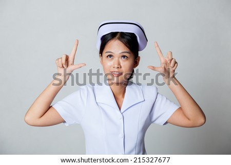 Young Asian nurse point up with both hands  and look up on gray background