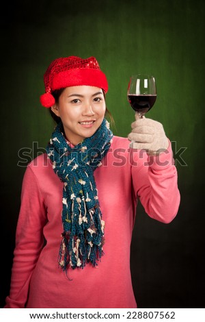 Asian girl wear christmas hat cheers with wine on dark green background
