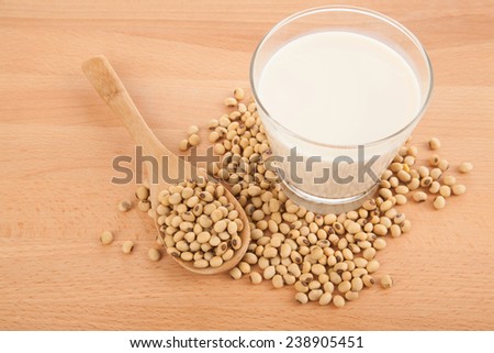 Soy milk in glass with soybeans and wooden spoon on wood table