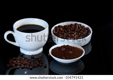 Cup of fresh brewed Coffee with plates of coffee beans and ground coffee.