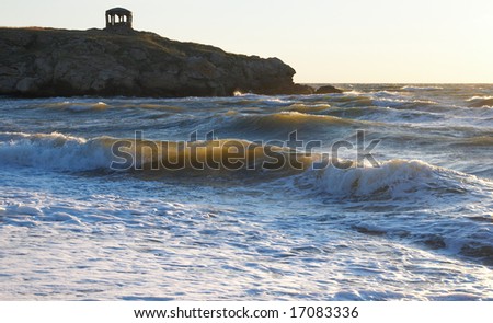 Sea surf great wave break on evening coastline and cape with pavilion at a distance