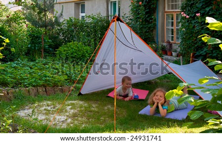 Two small children play in summer garden near their house