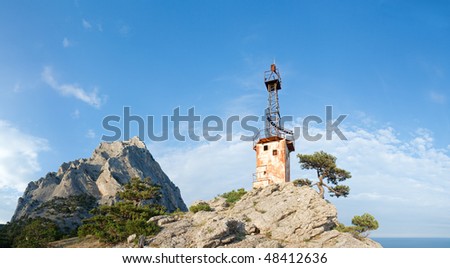 rock with conifer trees and old lighthouse on slope on blue sky background (\