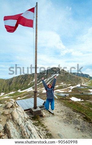 Austrian Flag above Alps mountain and Grossglockner High Alpine Road and jumping woman - tourist near