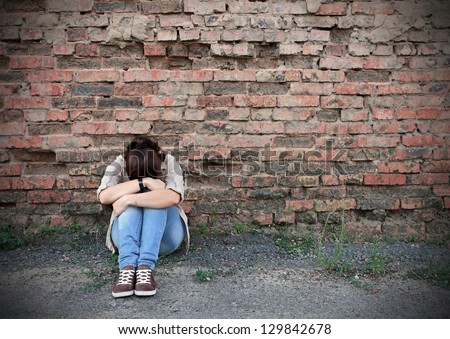 Young woman in despair sitting against a brick wall