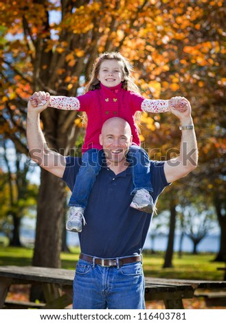 Daddy carrying daughter on shoulders in the fall