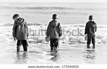Three boys paddling in the ocean in black and white