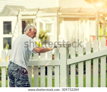 Active senior man painting a white picket fence with Instagram style filter
