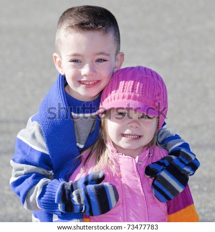 Cute brother and sister in winter hugging outside