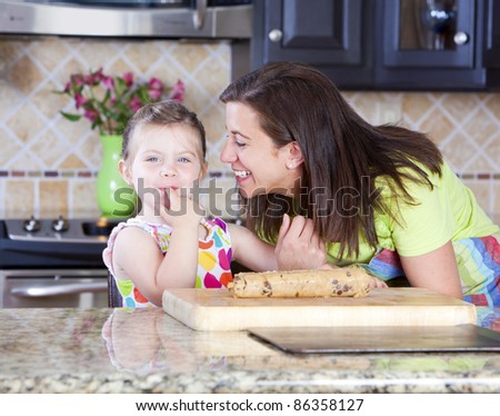 Mother and daughter putting cookie dough onto baking sheet in kitchen