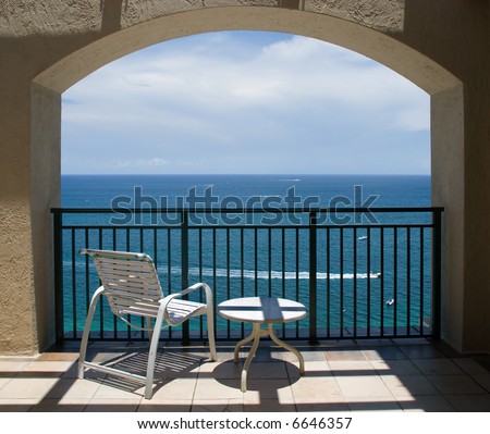An inviting view of the ocean and a boat through an arch of a balcony.