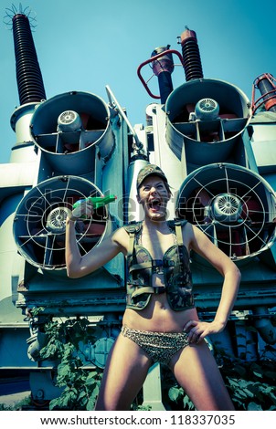 Woman in military camouflage shoots himself from a water pistol on the industrial background. Too hot to live concept.